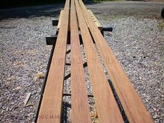 a long wooden bench sitting on top of a gravel field next to a forest filled with trees