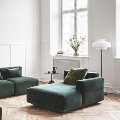 a green couch sitting in front of a window next to a table with a vase on it