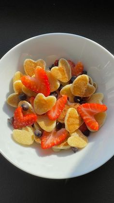 a white bowl filled with fruit and nuts on top of a black countertop next to a fork