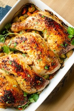 chicken with herbs in a white casserole dish on a wooden table top, ready to be eaten