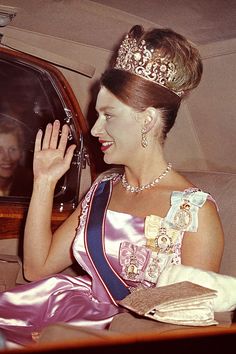 a woman in a tiara waves from the back seat of a car