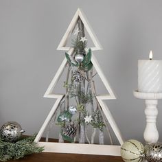 a white christmas tree sitting on top of a wooden table next to a lit candle