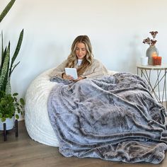 a woman is sitting on a bean bag chair with a blanket over her head and reading a book