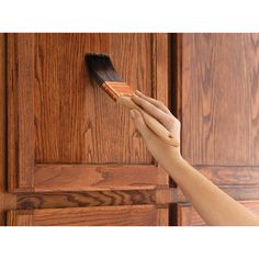 a person is holding a brush in their hand to paint the side of a wooden cabinet