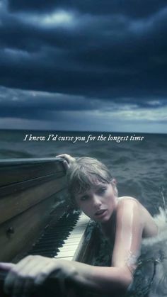 a woman sitting on top of a piano in the ocean under a dark cloudy sky