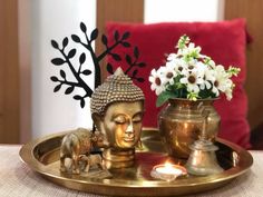 a small buddha statue sitting on top of a metal tray next to a vase filled with flowers