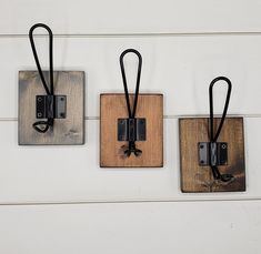 three square wooden plaques with black cords hanging from them on a white wood paneled wall