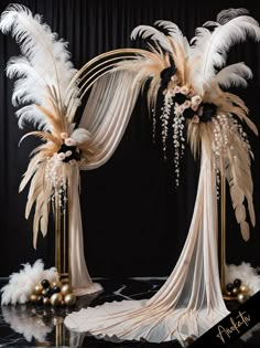 an elaborate wedding arch decorated with white feathers and black flowers, gold balls and pearls