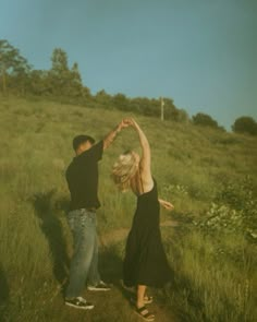 two people standing in the grass with their arms up and one person reaching for something