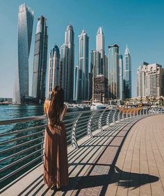 a woman standing on a bridge looking out over the water with tall buildings in the background