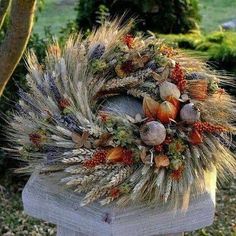 a wreath made out of dried flowers and leaves on top of a wooden post in the grass