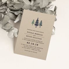 a wedding card with pine trees on it next to some greenery and leaves in front of a white background