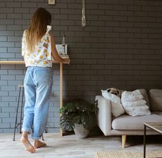 a woman standing in front of a white couch next to a table with a plant on it