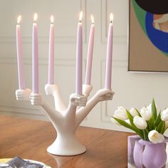 a table topped with lots of candles on top of a wooden table next to a vase filled with white flowers