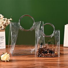 two clear acrylic bags sitting on top of a wooden table next to flowers