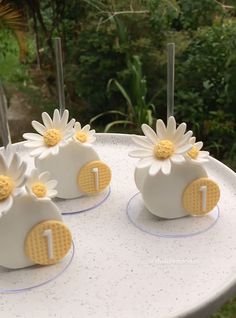 four white cakes with yellow and white flowers on them sitting on a table in front of some bushes