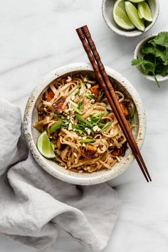 a bowl filled with noodles and vegetables next to chopsticks on a white table