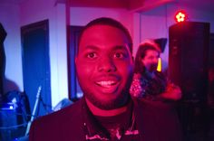 a man in a suit and bow tie smiling at the camera with other people behind him