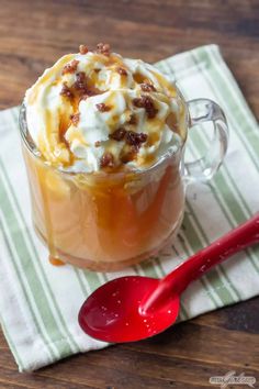 a glass mug filled with ice cream and caramel on top of a napkin next to a red spoon