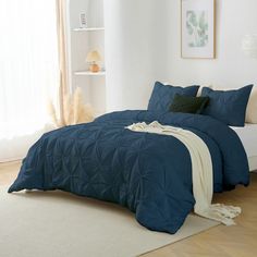 a bed with blue comforter and pillows in a white room