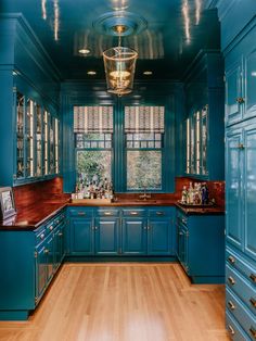 a blue kitchen with wooden floors and cabinets in the center is lit by a chandelier