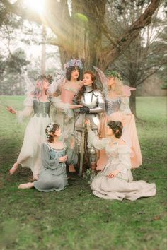 a group of women dressed in medieval costumes sitting under a tree with their arms around each other