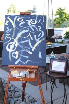 an easel with a painting on it in front of some rocks