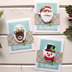 three christmas cards with santa claus, snowman and reindeer on them sitting next to evergreens