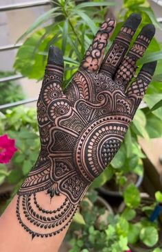 a hand with henna on it and some plants in the backgroung