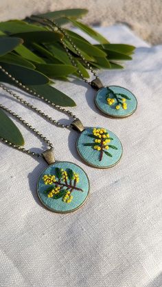 three necklaces with yellow flowers on them sitting next to some green leafy branches