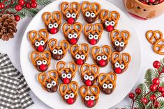 a white plate topped with pretzels covered in reindeer face cookies next to pine cones