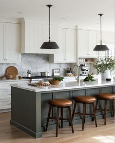 a kitchen island with three stools in front of it and two lights hanging from the ceiling