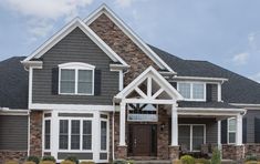 a large gray house with white trim and stone accents on the front porch, along with two car garages