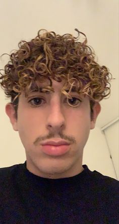 a man with curly hair and a moustache looks at the camera while wearing a black shirt