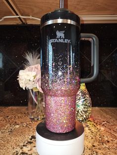 a purple and black tumbler sitting on top of a counter next to a vase