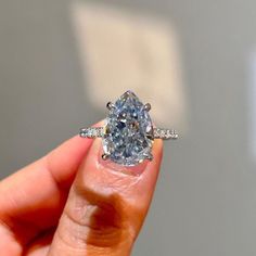 a woman's hand holding an engagement ring with a pear shaped diamond in it