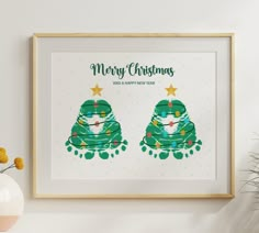 a framed christmas card with two green cartoon characters on the front and bottom, sitting next to a potted plant