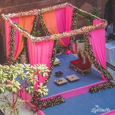 an outdoor wedding setup with pink and orange draping on the stage, surrounded by greenery