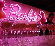 several martini glasses lined up in front of a neon sign with the word barbie's on it