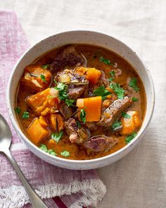 a bowl of stew with carrots, meat and parsley in it on a table