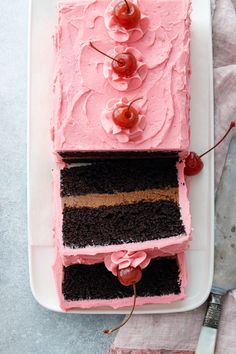 a square cake with pink frosting and cherries on top, sitting on a plate