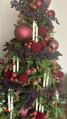 a christmas tree decorated with red and gold ornaments, pine cones, candles and berries