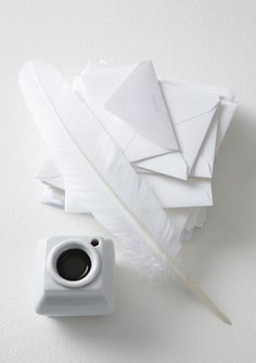 a cup of coffee sitting next to some white papers and a feather on top of it