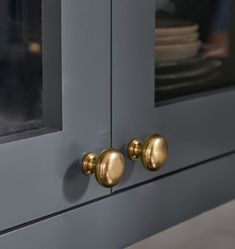 two brass knobs on the side of a gray cabinet with plates stacked in it