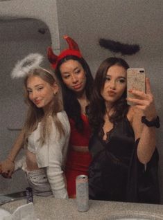 three women taking a selfie in the bathroom with devil horns on their head and one holding a cell phone