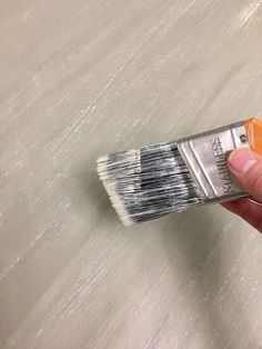 a hand holding a paintbrush with white bristles on top of it and the brush has an orange tip