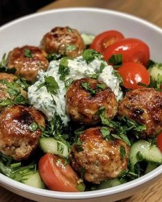 a white bowl filled with meatballs, cucumbers and tomatoes on top of lettuce