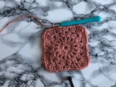 a crocheted square is sitting on a marble surface with a hook in the middle