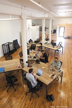 people working on their laptops in an open office space with hard wood flooring