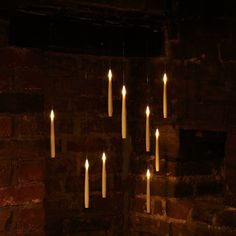 many lit candles hanging from the ceiling in a dark room with brick walls and exposed lighting